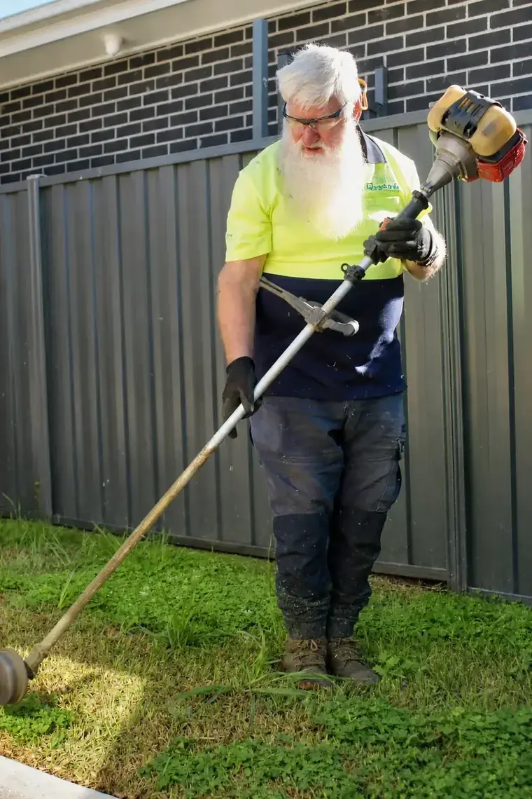 Line trimming long overgrown grass against a fence during a garden clean-up